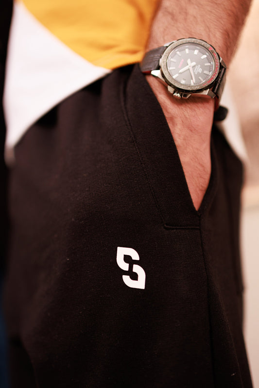 Person wearing a black polo shirt with a white logo and a yellow and white shirt underneath, focusing on the watch.