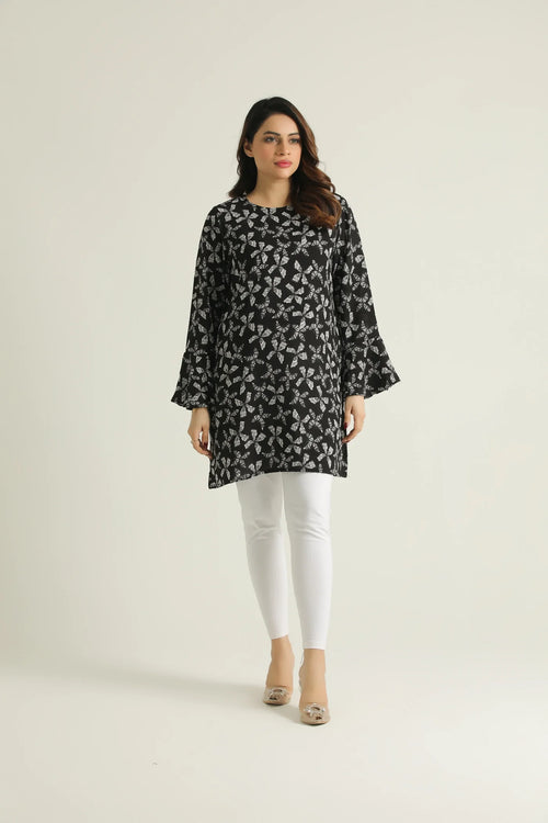 A woman wearing a mid-length printed top with bell sleeves and a round neckline, paired with white pants.