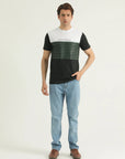 A man standing against a white background wearing a round-neck, striped t-shirt and blue jeans.