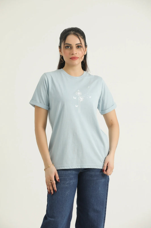 A woman wearing a pastel blue printed t-shirt with round neck, binding, contrast print, and turn-up half sleeves, paired with blue jeans.