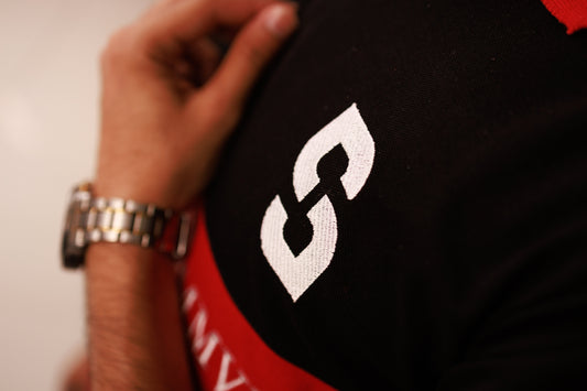 Close-up of a black and red shirt with a white logo, worn by a person with a watch.