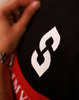 Close-up of a black and red shirt with a white logo, worn by a person with a watch.