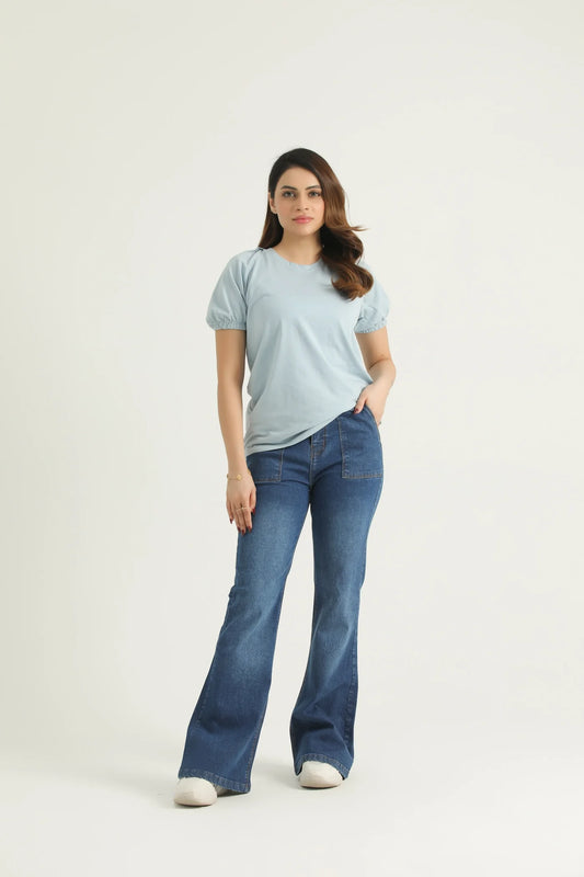 A woman wearing a pastel blue knit top with a round neck, raglan sleeves, and elasticated half sleeves, paired with blue jeans.