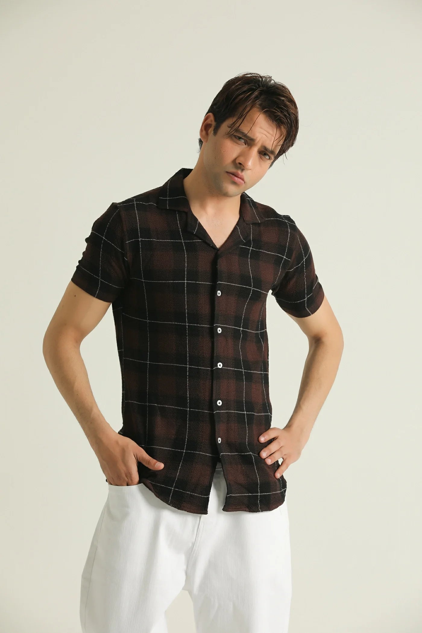 A man wearing a short-sleeved textured check shirt in red and blue plaid with a resort collar, white pants, and brown shoes.