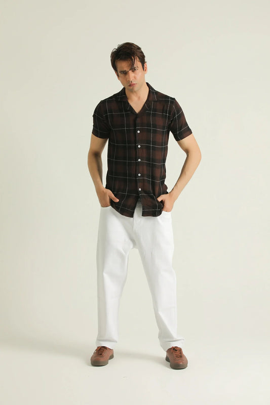 A man wearing a short-sleeved textured check shirt in red and blue plaid with a resort collar, white pants, and brown shoes.