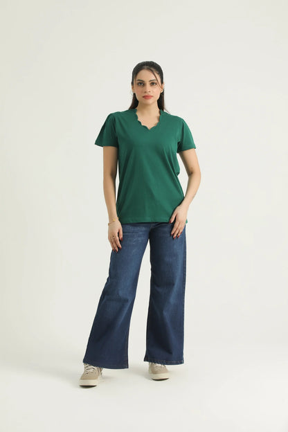 A woman wearing a green scalloped neck knit top with half sleeves, paired with blue jeans and beige shoes.