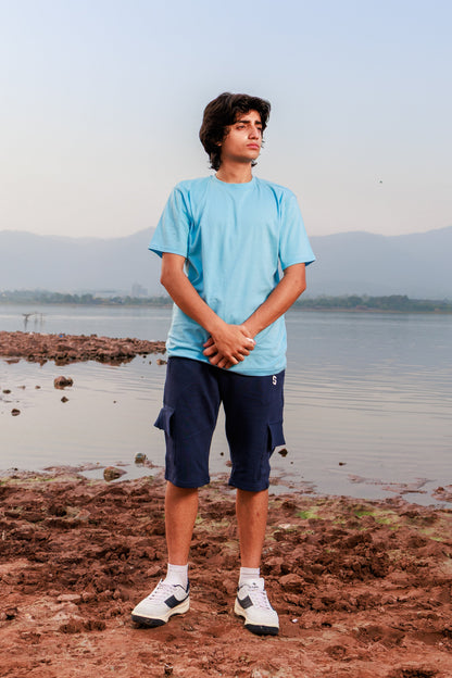 Person standing on a rocky shore with water and mountains in the background
