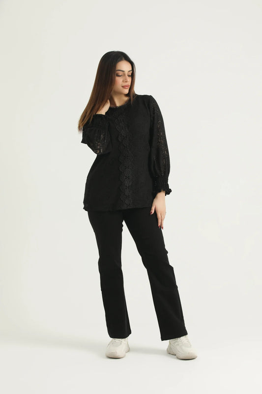 A woman standing against a white background wearing black straight leg denim jeans and a black top with long sleeves.