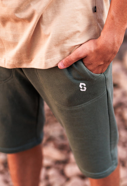 Person wearing green shorts with a logo on a blurred natural background
