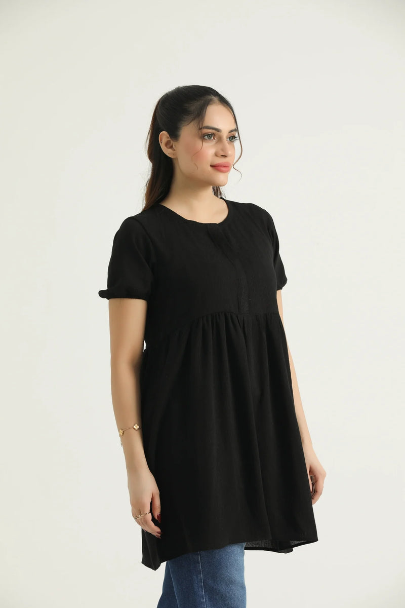 A model wearing a mid-length dark saddle top with short sleeves and a round neckline, made of georgette weave fabric.