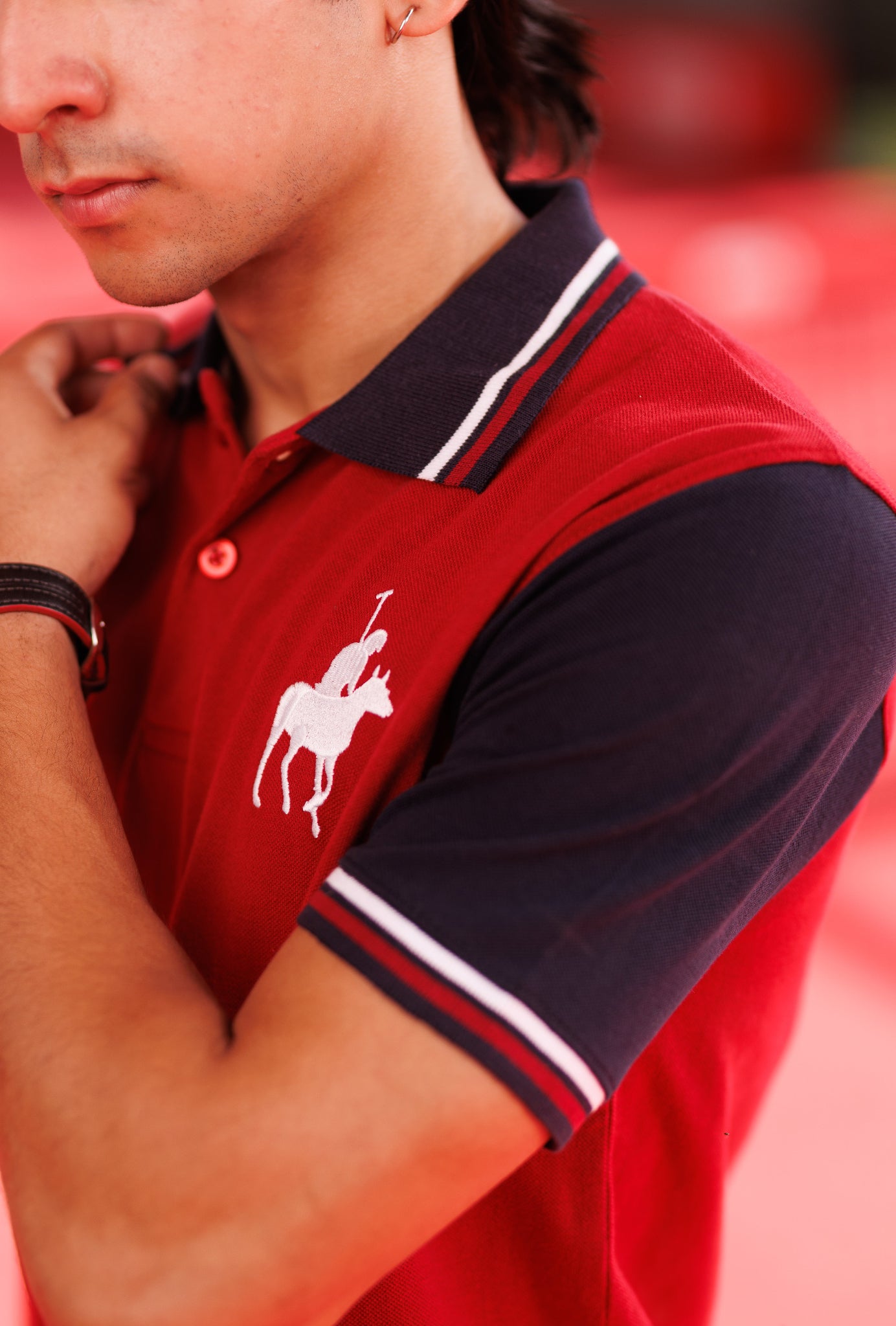 Red polo shirt with a white logo worn by a person against a blurred red background