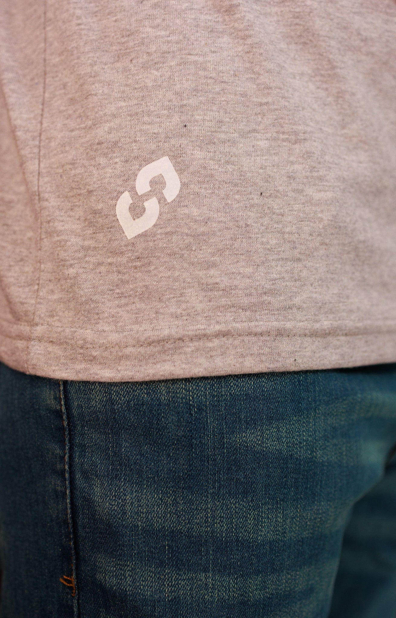 Close-up of a brown hoodie with a logo worn over blue jeans.