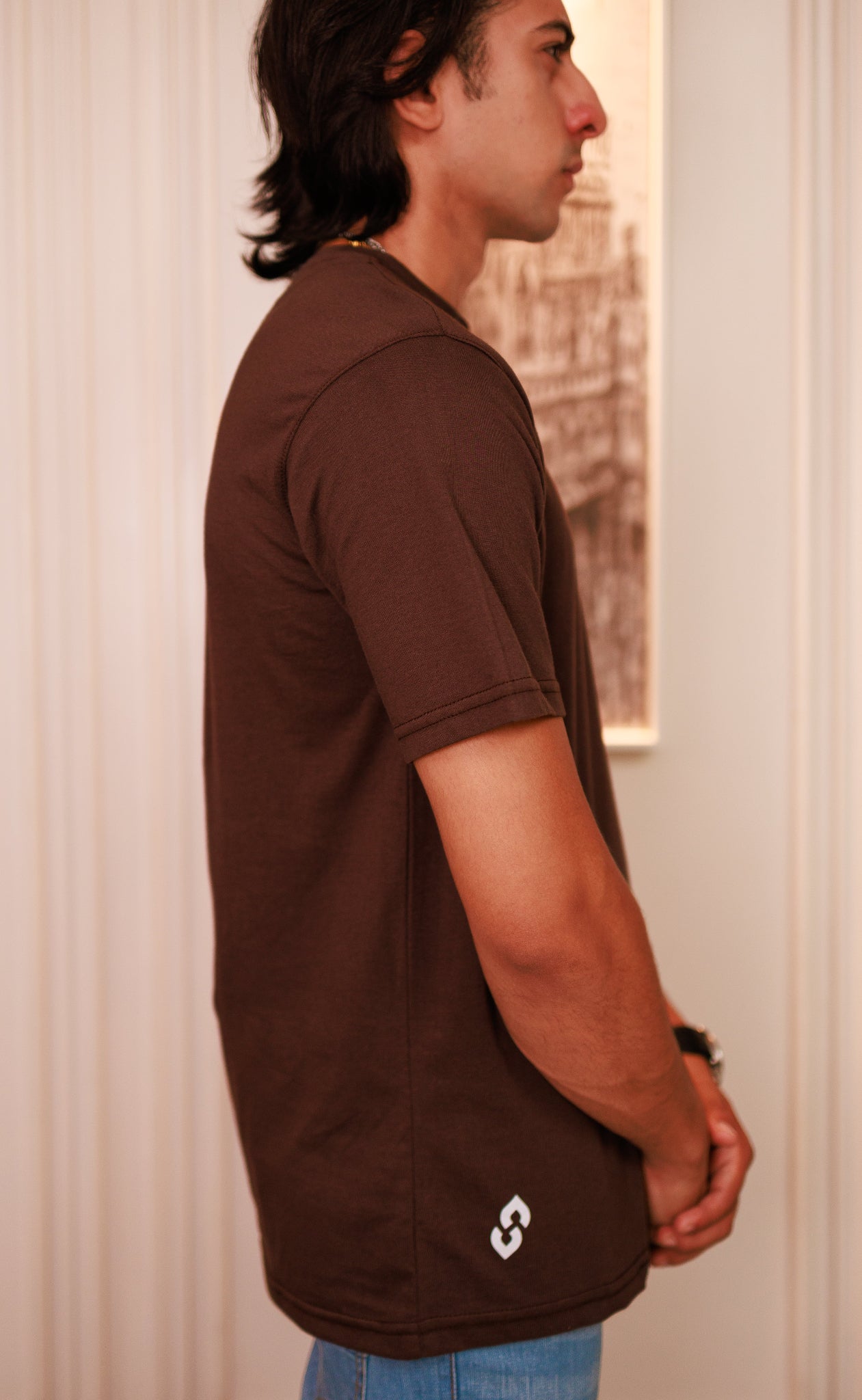 Person wearing a brown t-shirt with a logo, standing indoors.