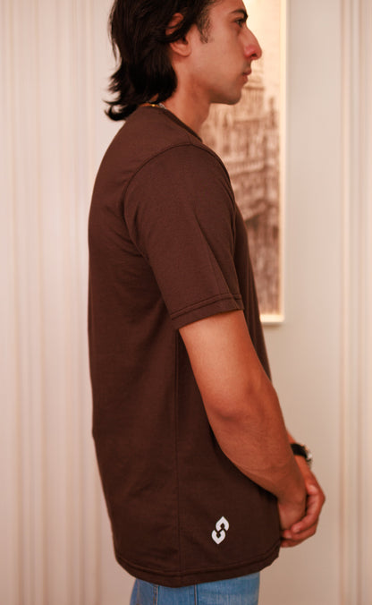 Person wearing a brown t-shirt with a logo, standing indoors.