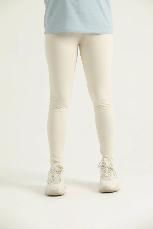 A pair of beige leggings on a female model, paired with a blue top and white sneakers.