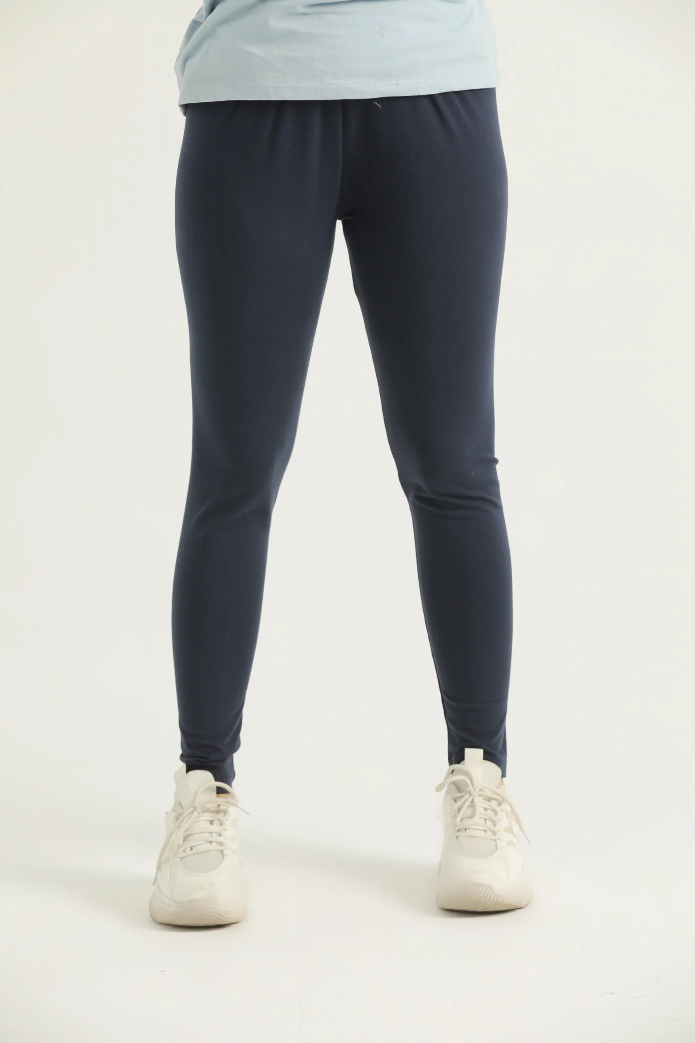 A pair of navy blue leggings on a female model paired with a blue top and white sneakers, standing against a white background.