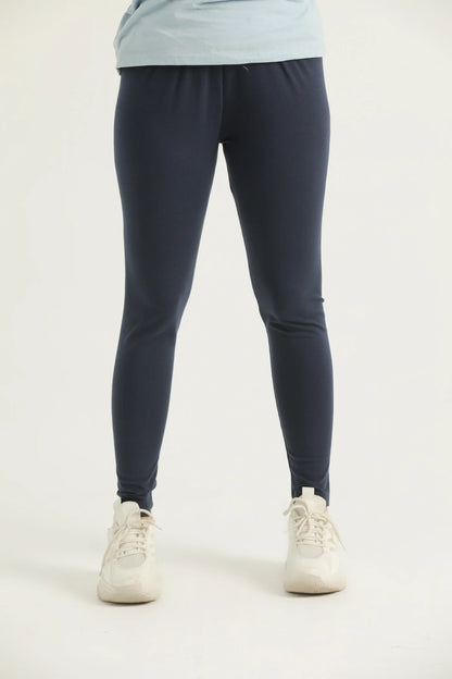 A pair of navy blue leggings on a female model paired with a blue top and white sneakers, standing against a white background.