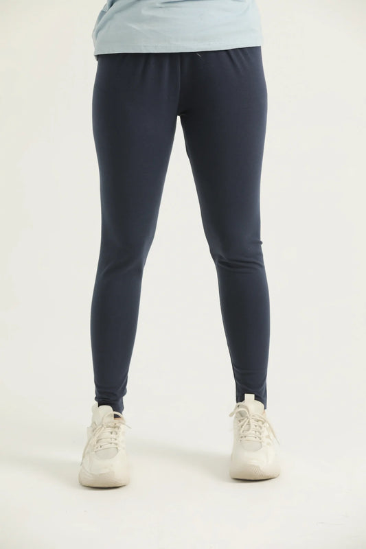 A pair of navy blue leggings on a female model paired with a blue top and white sneakers, standing against a white background.