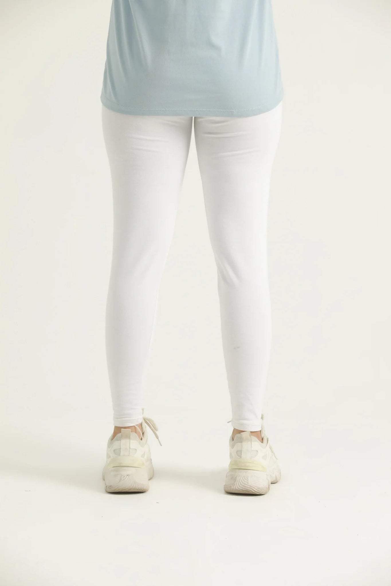 Person wearing a light blue top and white pants on a plain background