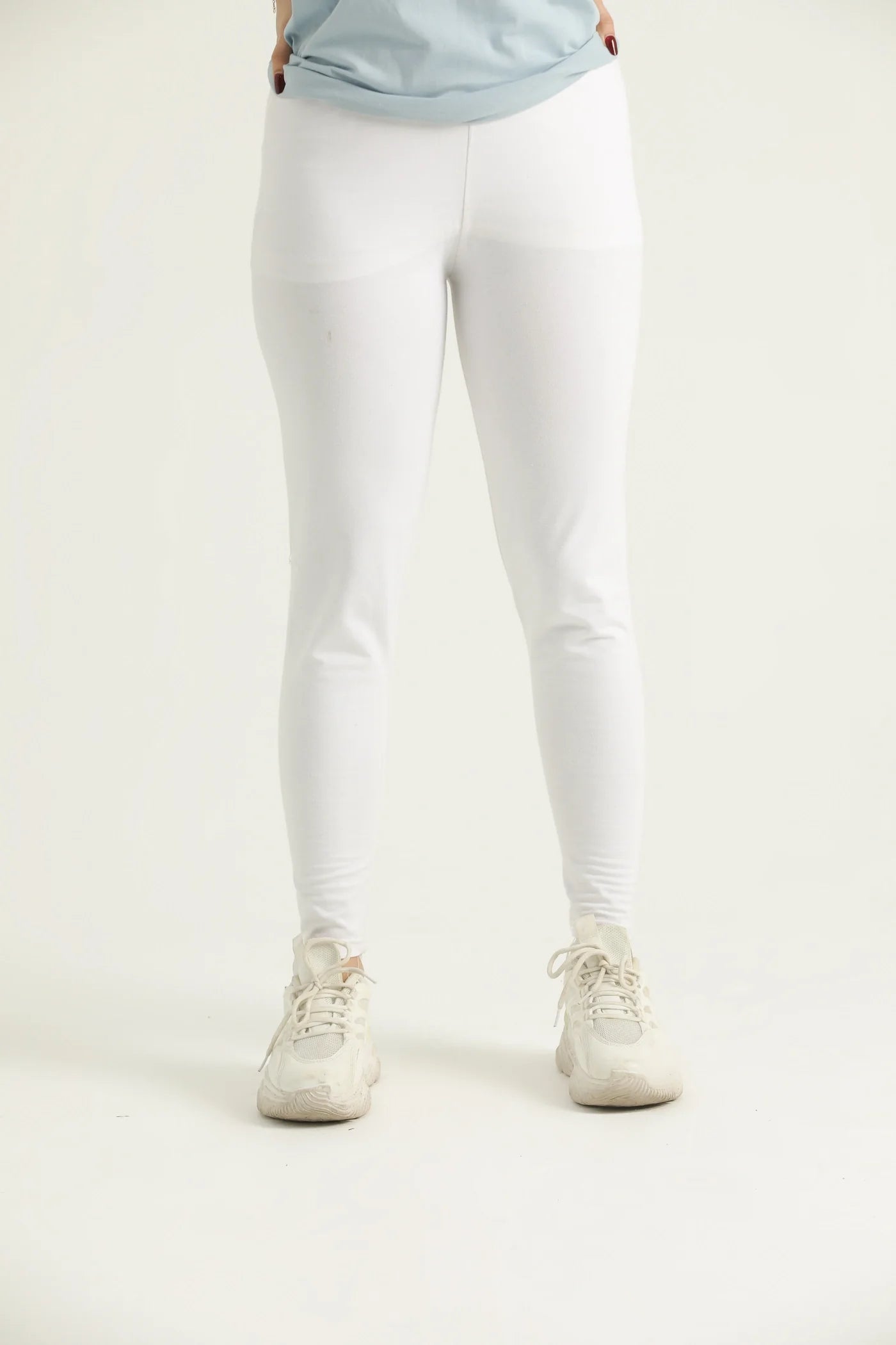 A pair of white leggings on a female model paired with a blue top and white sneakers.