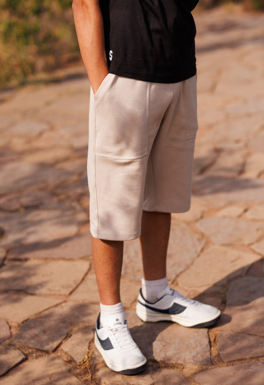 Person wearing beige shorts and white sneakers on a stone pavement