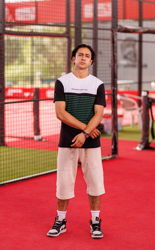 Person standing on a red sports court wearing a black and white striped shirt and beige shorts.
