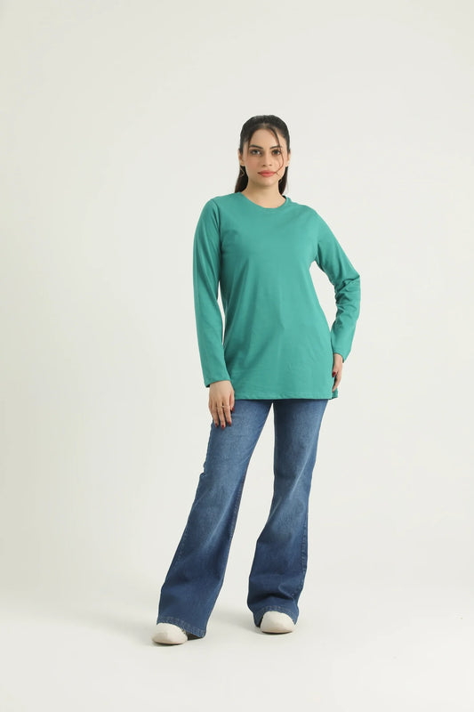 A woman standing against a white background wearing a long sleeve knit top in green and blue jeans.