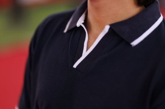 Navy polo shirt with white trim worn by a person on a blurred background