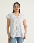 A woman wearing a white v-neck top with lace details and cap sleeves, paired with blue jeans.