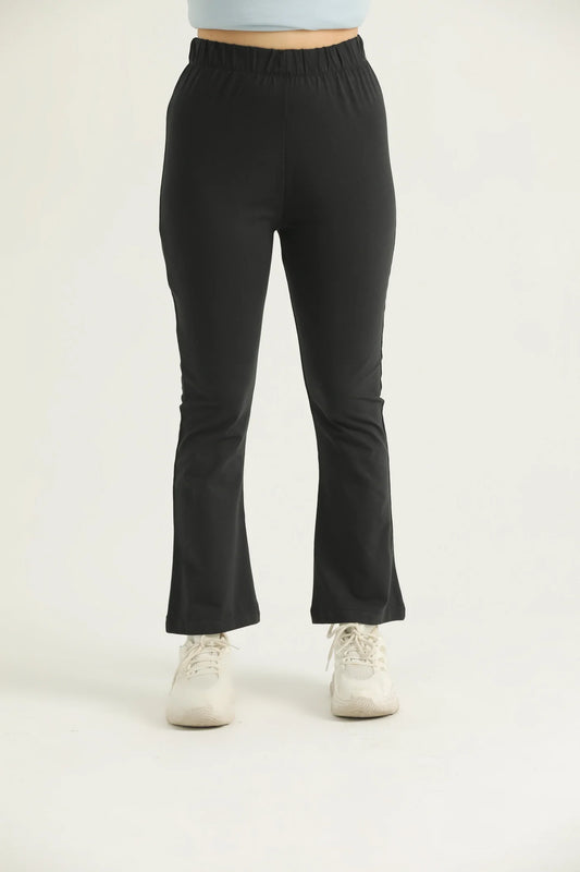 A pair of black flared leggings with a high waistband, modeled by a woman standing against a white background