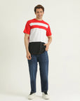 A man wearing a red and white striped t-shirt with a round, rib-trimmed neckline and a straight-cut hem, paired with blue jeans and white sneakers.