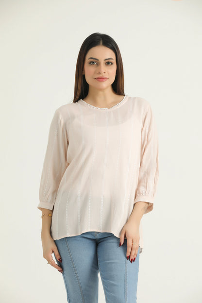 A woman wearing a beige, self-embroidered, 3/4 length bishop sleeve top with a round neckline and a back slit opening, paired with blue jeans.