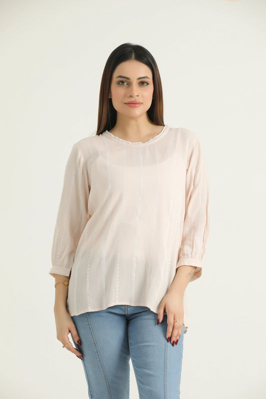 A woman wearing a beige, self-embroidered, 3/4 length bishop sleeve top with a round neckline and a back slit opening, paired with blue jeans.