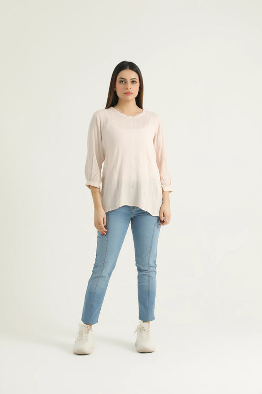 A woman standing, wearing a beige tank top with a round neck and back slit opening, paired with blue jeans and white shoes.