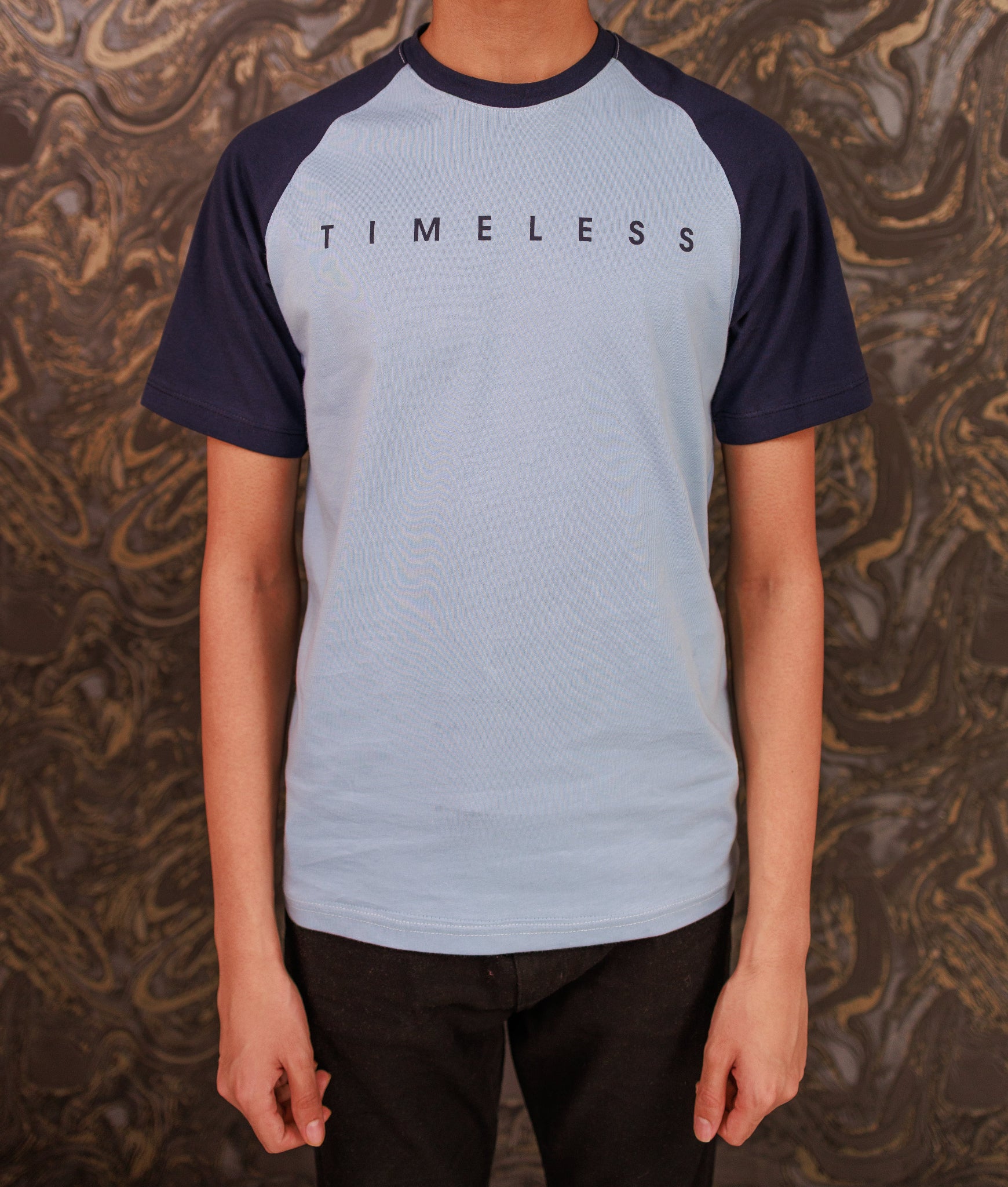 Person wearing a blue and navy 'TIMELESS' t-shirt against a patterned background
