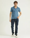 A man wearing a blue short-sleeved polo shirt with a collar, and blue jeans.