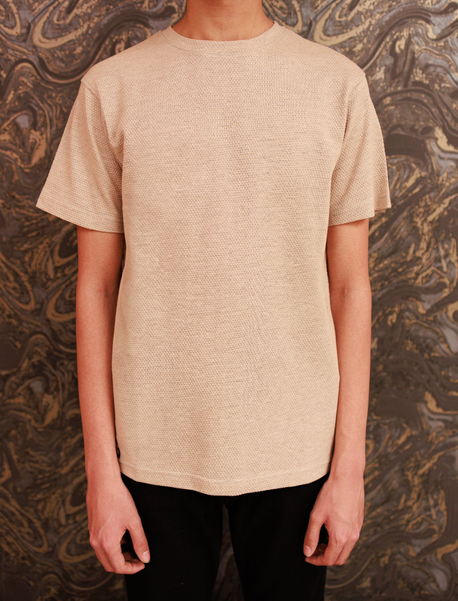 Person wearing a beige textured t-shirt against a patterned background