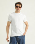 A man wearing a white crew neck t-shirt and blue jeans.