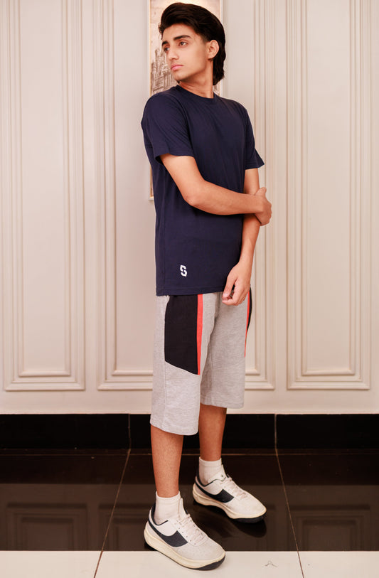 Person wearing a navy blue t-shirt and gray shorts with a colorful design, standing in a room with white paneled walls.