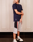 Person wearing a navy blue t-shirt and gray shorts with a colorful design, standing in a room with white paneled walls.