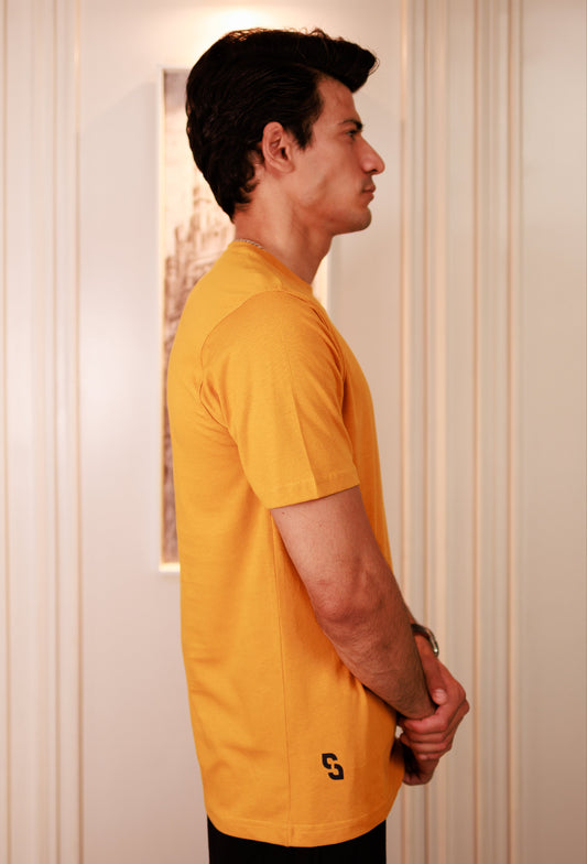 Man wearing a yellow t-shirt standing against a neutral wall.