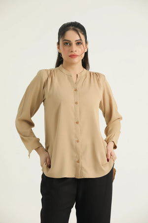 A woman wearing a beige button-down hip length top with long sleeves, buttoned placket, and rounded bottom hem.
