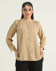 A woman wearing a beige button-down hip length top with long sleeves, buttoned placket, and rounded bottom hem.