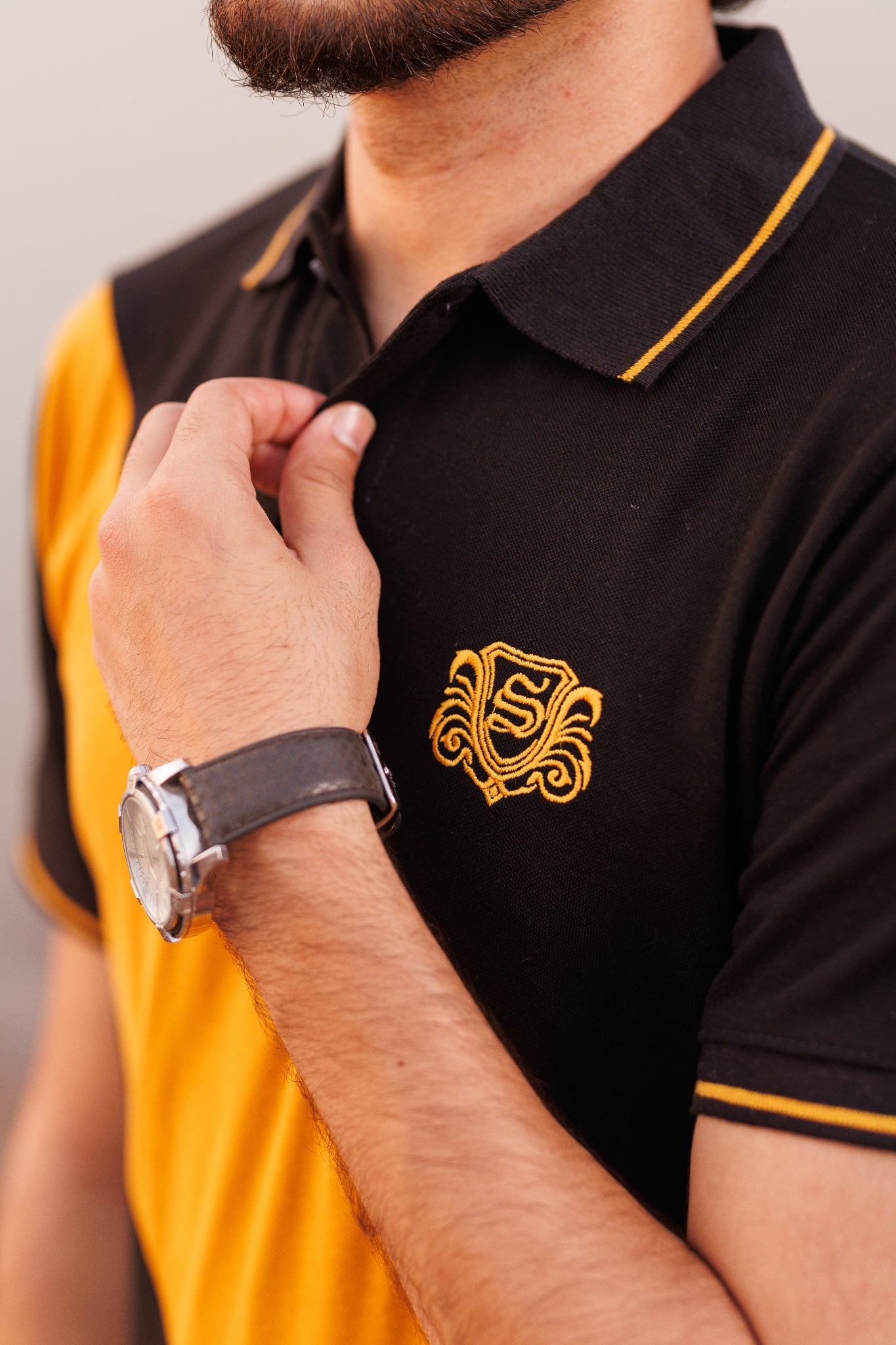 Person wearing a black and yellow polo shirt with a logo, close-up on the chest area.