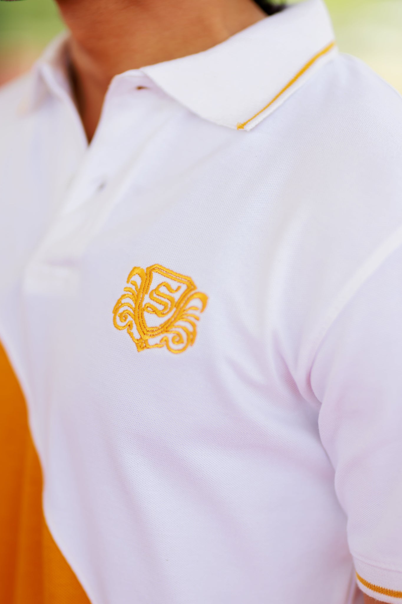 Close-up of a white polo shirt with a yellow logo and trim.