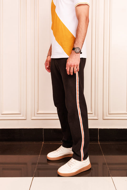 Person wearing black pants with a white and orange stripe, white shirt, and white shoes in a room.