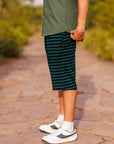 Person wearing green shorts with black stripes on a stone path with greenery in the background