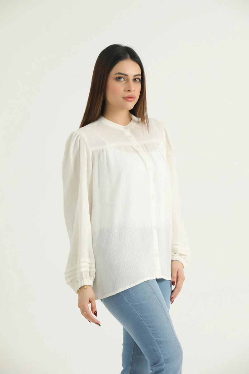 A woman wearing a white, long-sleeved, button-down top with a relaxed fit, made of slightly sheer fabric, paired with blue jeans.