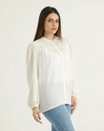 A woman wearing a white, long-sleeved, button-down top with a relaxed fit, made of slightly sheer fabric, paired with blue jeans.