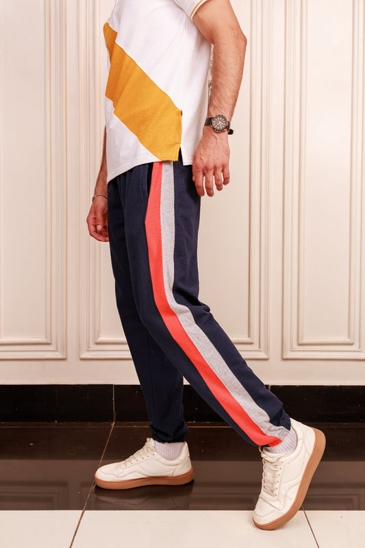 Person wearing navy jogger pants with colorful stripes, white shirt, and white sneakers indoors.